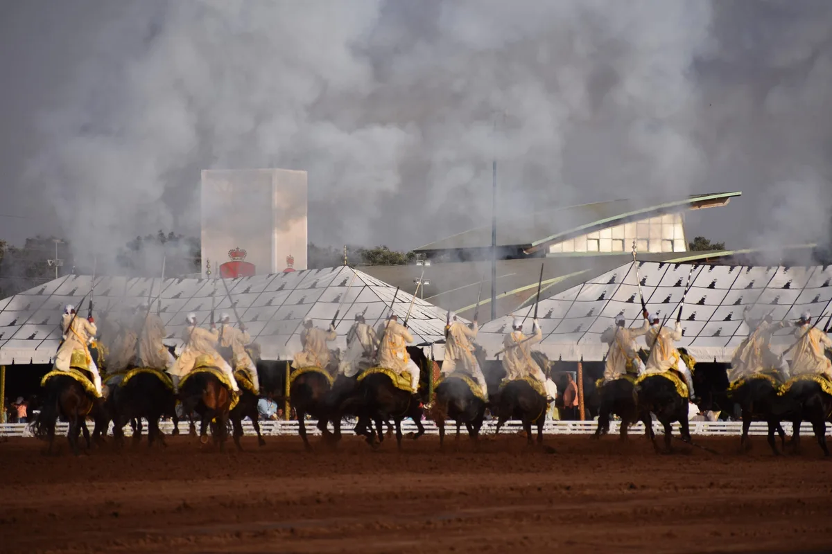 A line of Moroccan horsemen in traditional dress charging through clouds of gunpowder smoke and dust during a Tbourida fantasia
